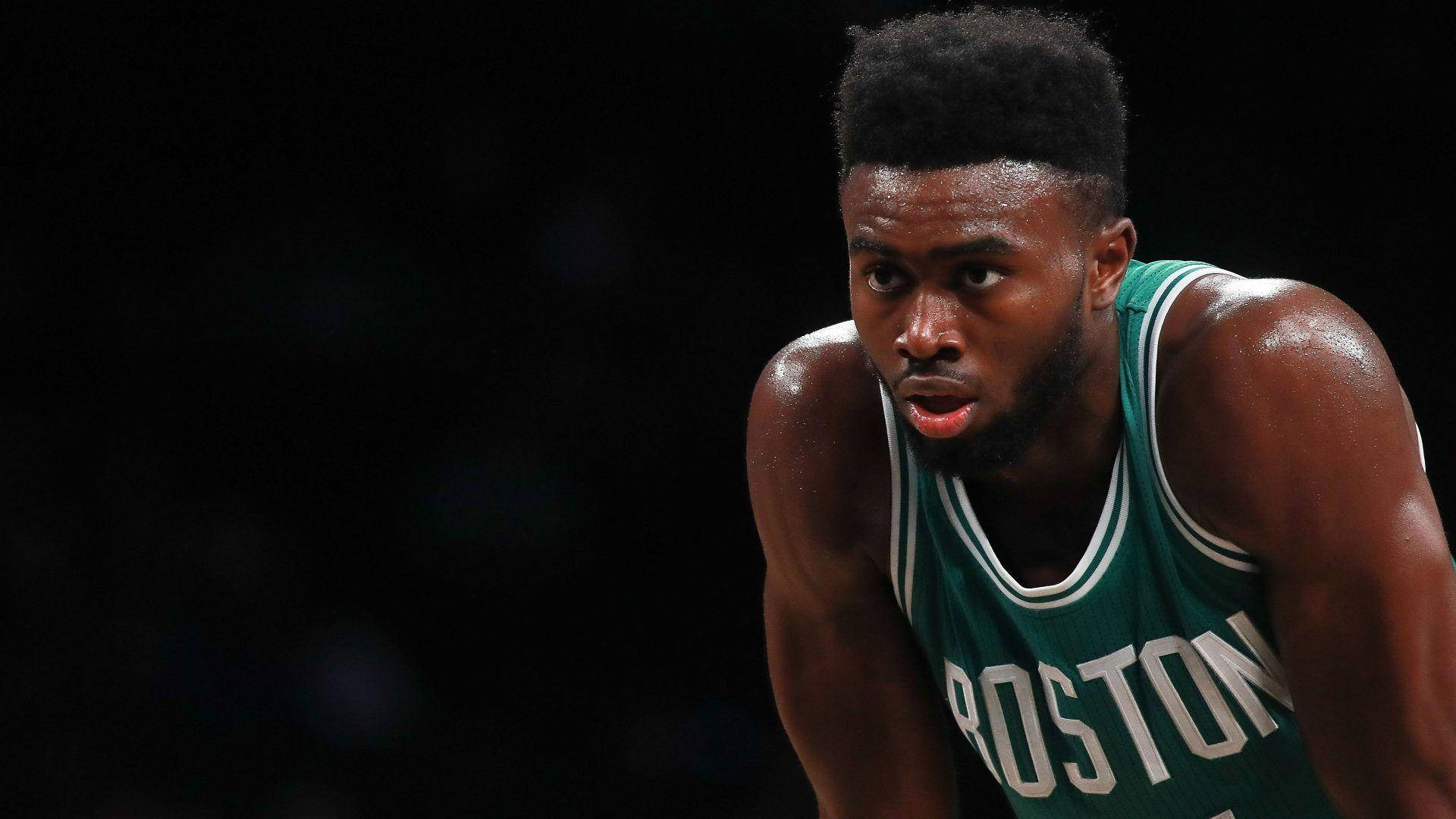 Jaylen Brown 黑色背景 壁紙 — 一位身穿綠色波士頓球衣的專注籃球運動員，在場館燈光下汗水閃閃發光，身體前傾。