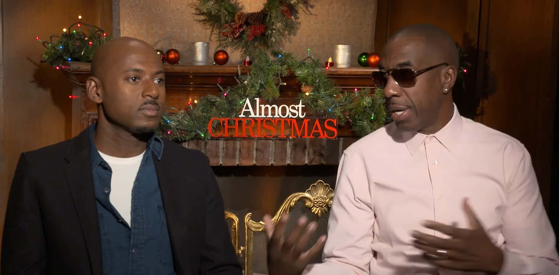羅曼尼·馬爾科與JB·斯穆夫在《Almost Christmas》節目中 壁紙 — 兩個男人坐在一個溫暖照明的房間裡，房間裝飾著聖誕節的彩帶和燈光在他們身後。