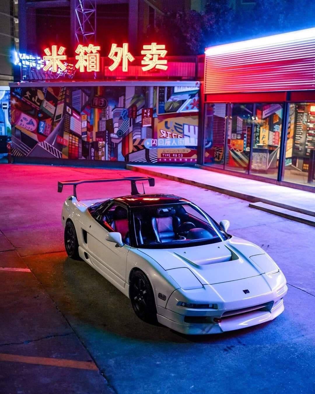 夜間停泊在霓虹燈照亮的都市街道上的白色跑車。