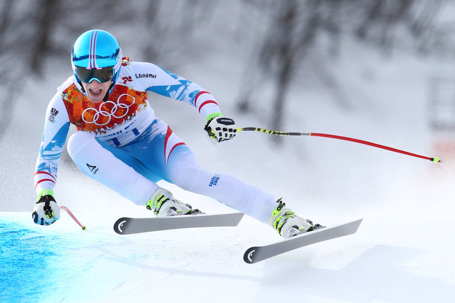 高山滑雪 Jean Claude Killy 壁紙 — 一名身穿藍白裝備的滑雪運動員在明亮的冬季斜坡上，以強烈的專注力和速度在雪中劃過。