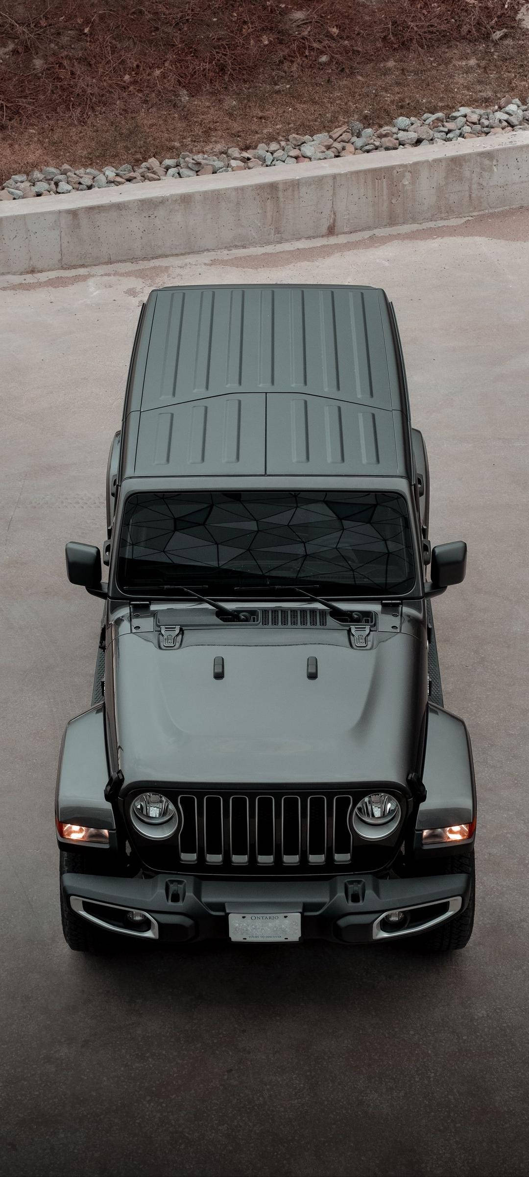 黑色 Jeep 高空俯瞰 壁紙 — 從上方俯瞰一輛啞光灰色Jeep Wrangler停在混凝土上，背景有碎石和混凝土牆。