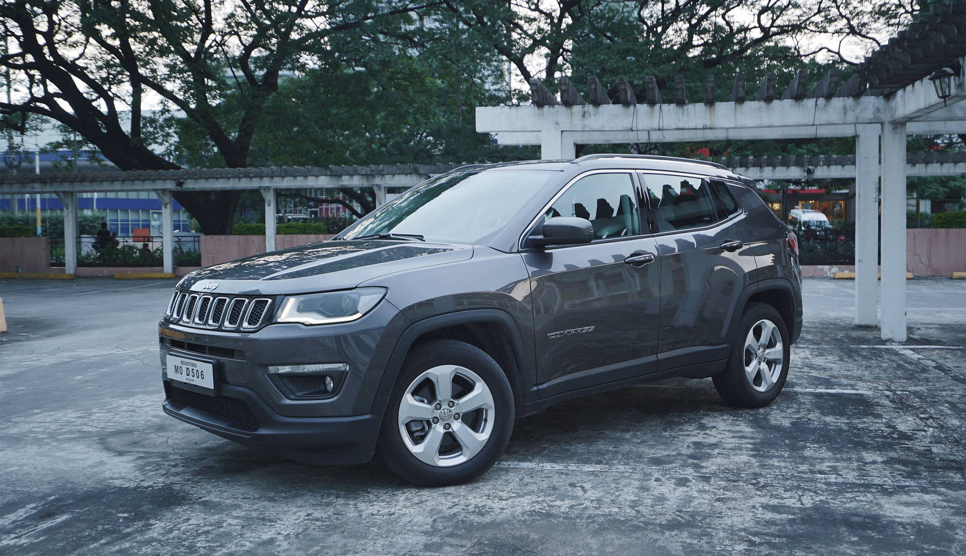 灰色Jeep Compass SUV停泊在市區停車區的樹下。