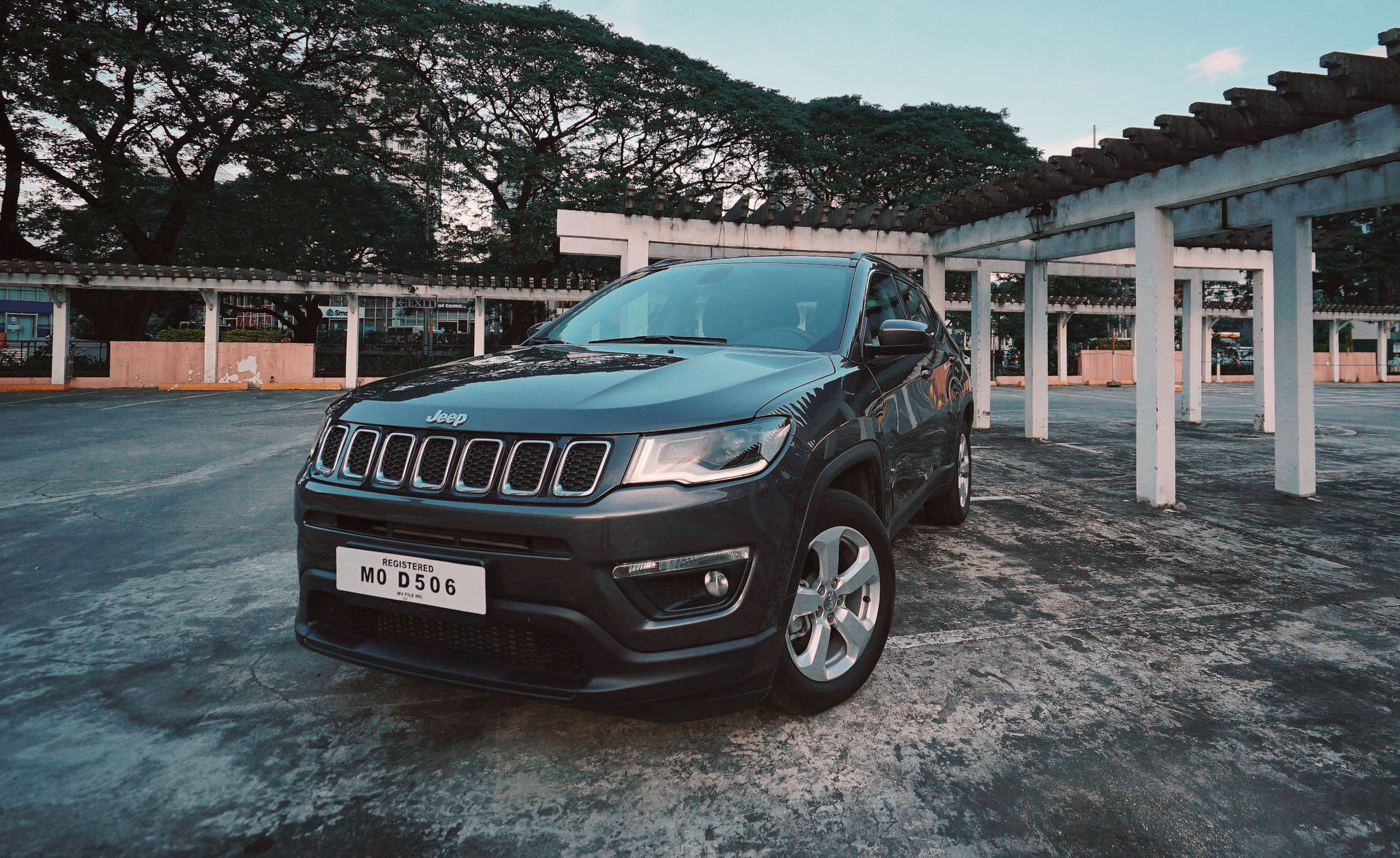 黑色Jeep Compass停放在有蓋結構下，背景有樹木。