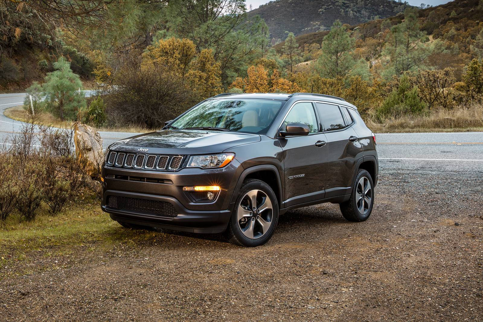 深灰色Jeep Compass停泊在秋日山丘彎路附近的碎石上。