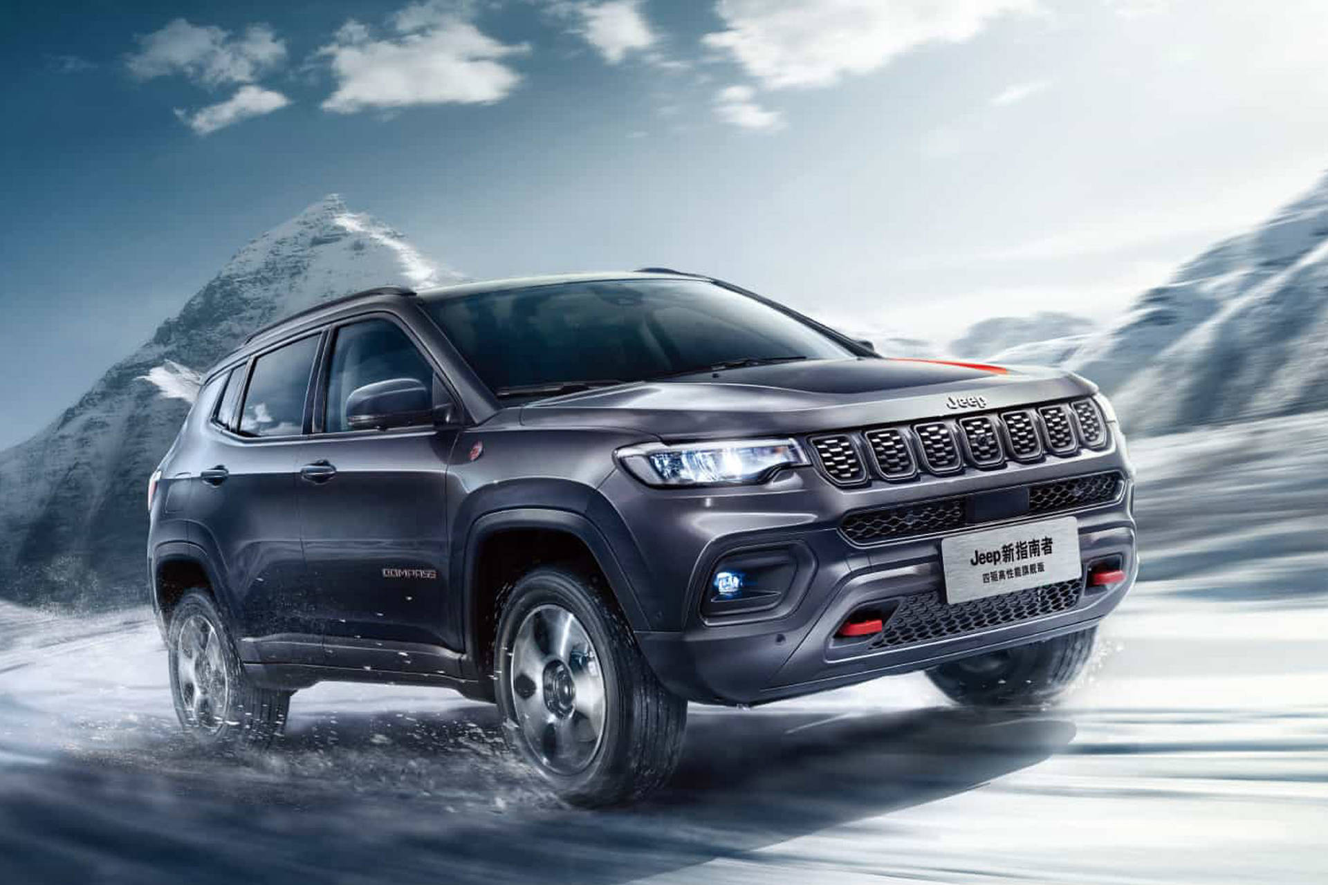 深灰色Jeep Compass在雪地中行駛，背景有山脈。