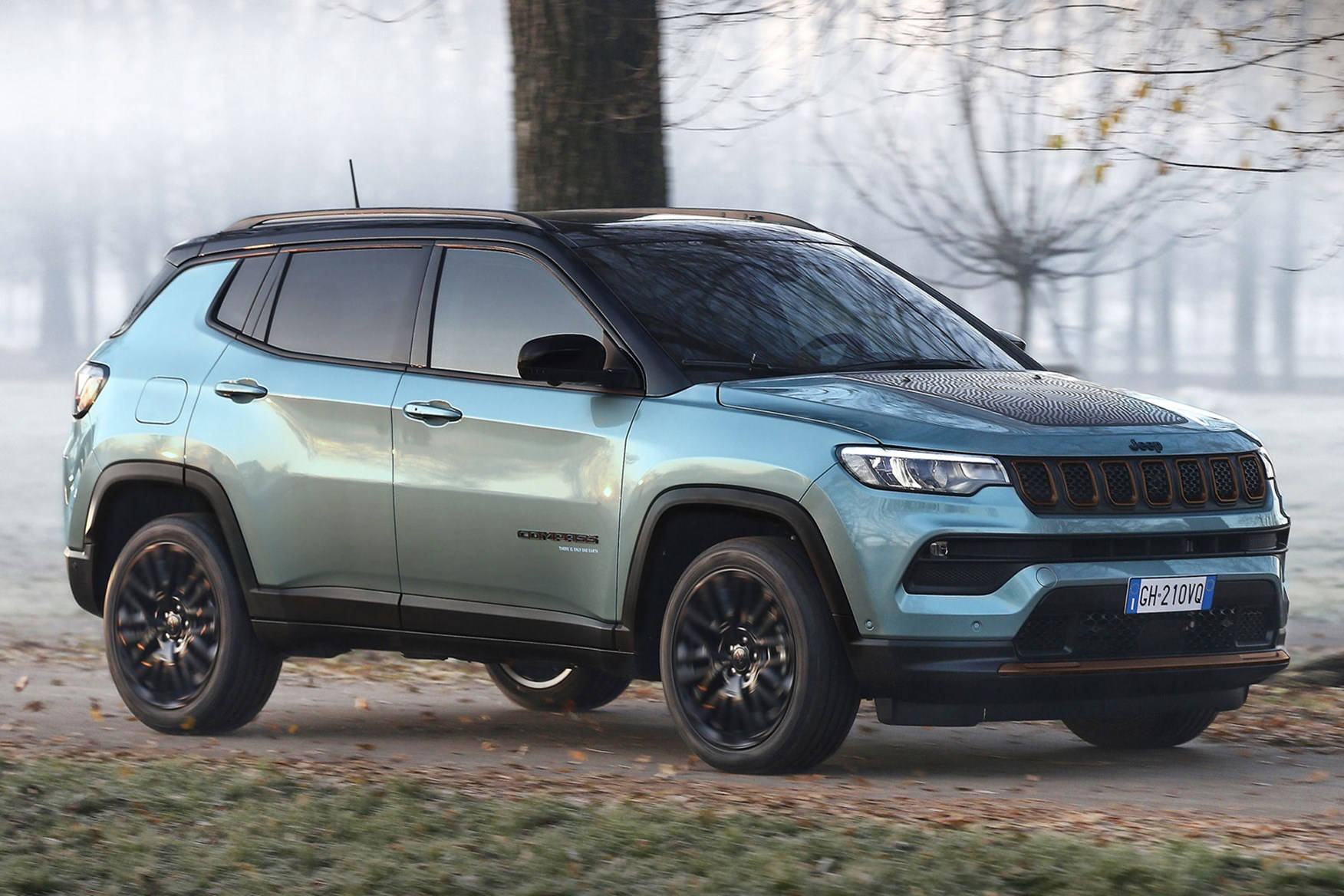 淺藍色Jeep Compass SUV停泊在霧氣瀰漫的秋日路邊，周圍有光禿的樹木。