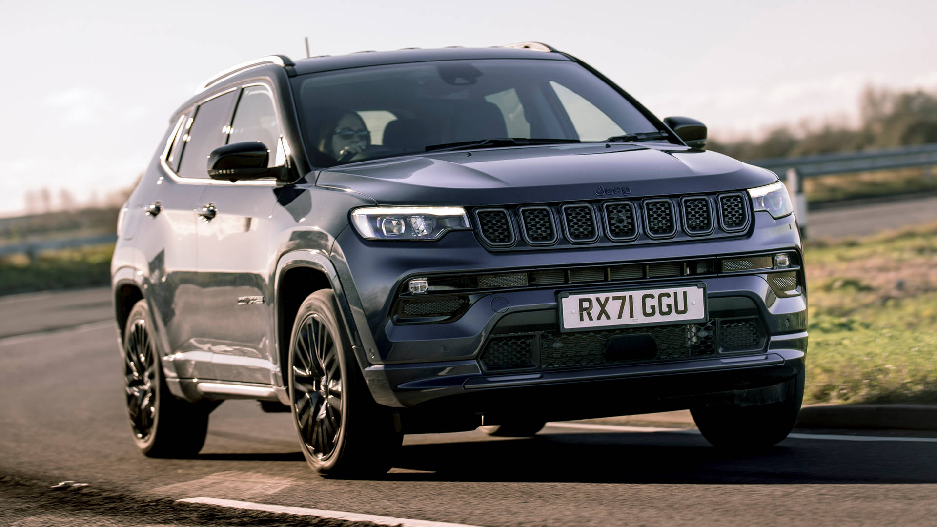 深藍色Jeep Compass SUV在鋪砌的道路上行駛，周圍有草地。