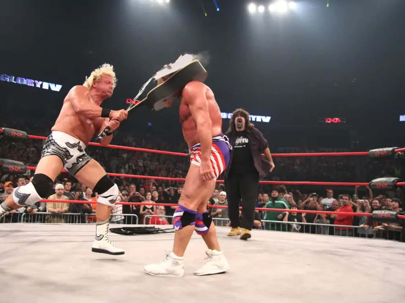 Jeff Jarrett WWE吉他砸擊對手攝影 壁紙 — 金髮摔角手在燈光明亮的擂台上向對手揮舞鋼椅，觀眾在旁觀看。