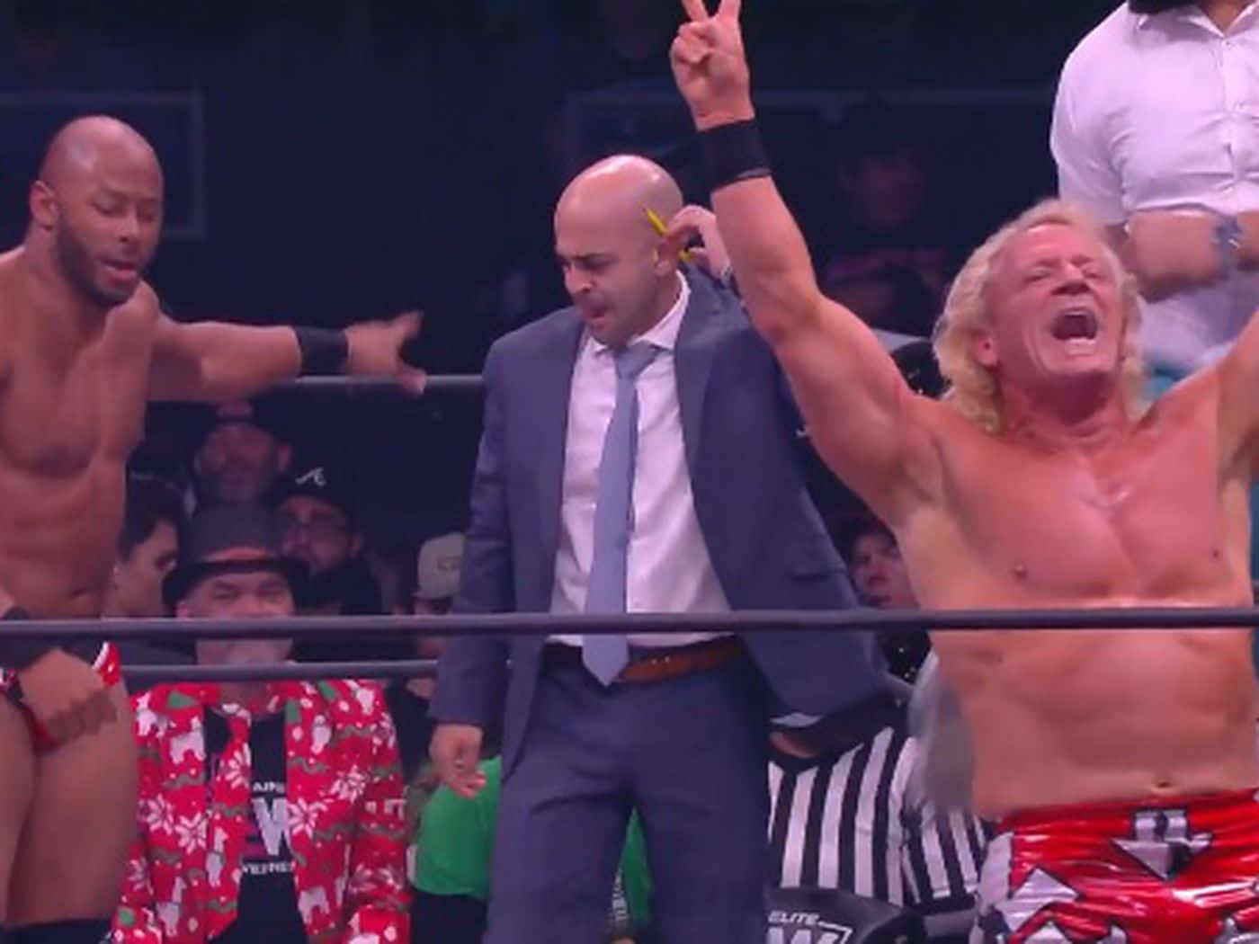 Jeff Jarrett WWE勝利慶祝攝影 壁紙 — 一位身穿紅色短褲的勝利摔角手高舉雙臂慶祝勝利，裁判和對手在座無虛席的場館中注視著。
