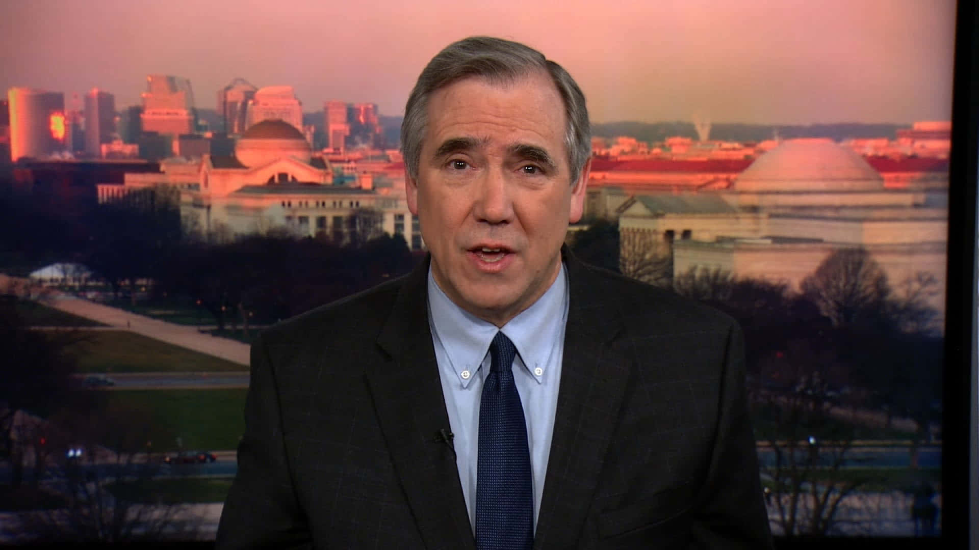 參議員 Jeff Merkley 激情演講 壁紙 — 一位身穿西裝的新聞主播在華盛頓特區地標前發言，背景沐浴在溫暖的夕陽色調中。