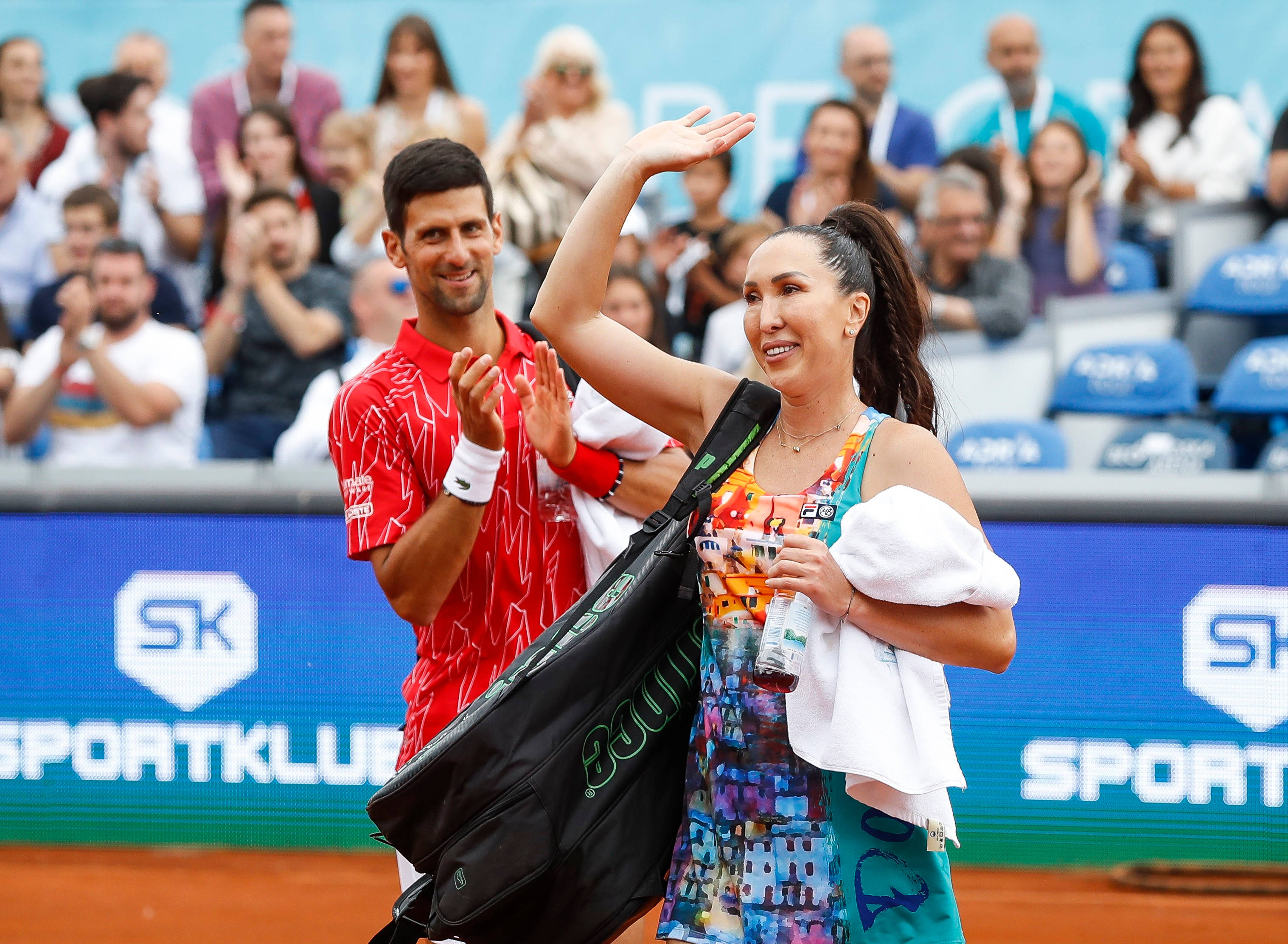 Jelena Janković向觀眾揮手 壁紙 — 網球選手在明亮的日光下向泥地球場上歡呼的人群揮手。