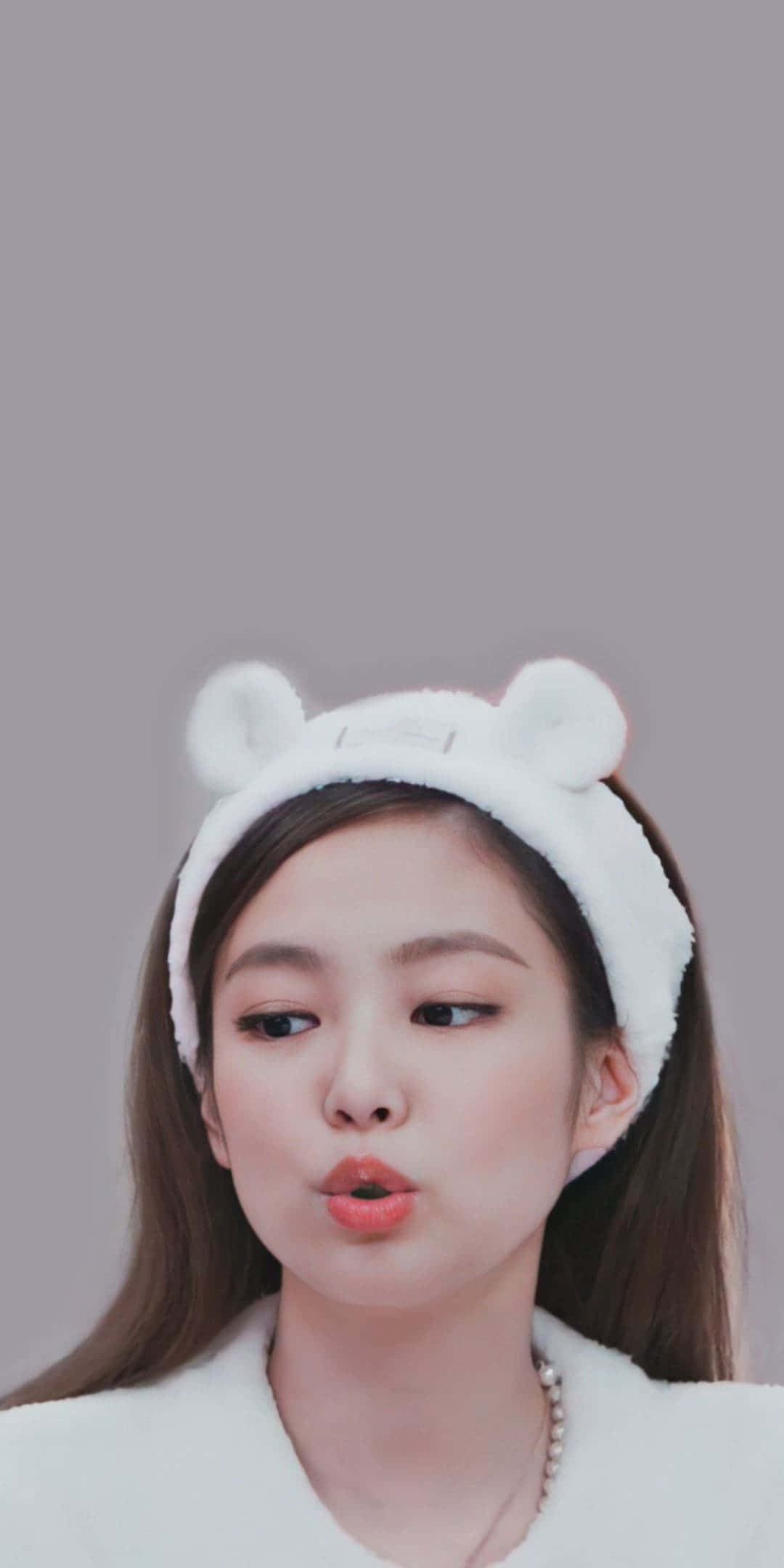 Jennie BLACKPINK 戴動物耳朵髮帶照 壁紙 — 一位年輕的棕髮女性戴著毛茸茸的白色熊耳頭帶，在純灰色背景前做出俏皮的嘟嘴表情。