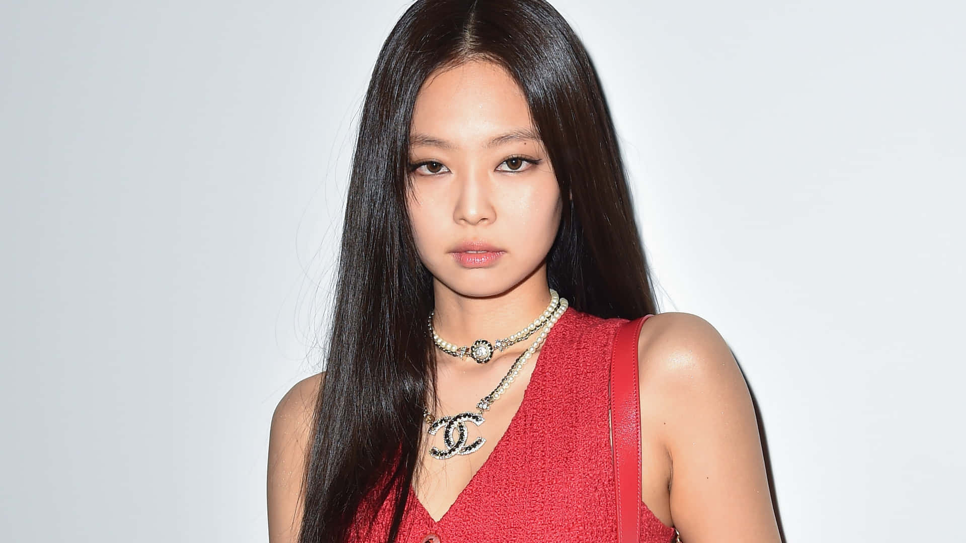 Jennie BLACKPINK 穿紅裙照 壁紙 — 一位長黑髮的優雅女士，身穿紅色質感上衣，配搭多層次的 Chanel 首飾，背景為純白色。
