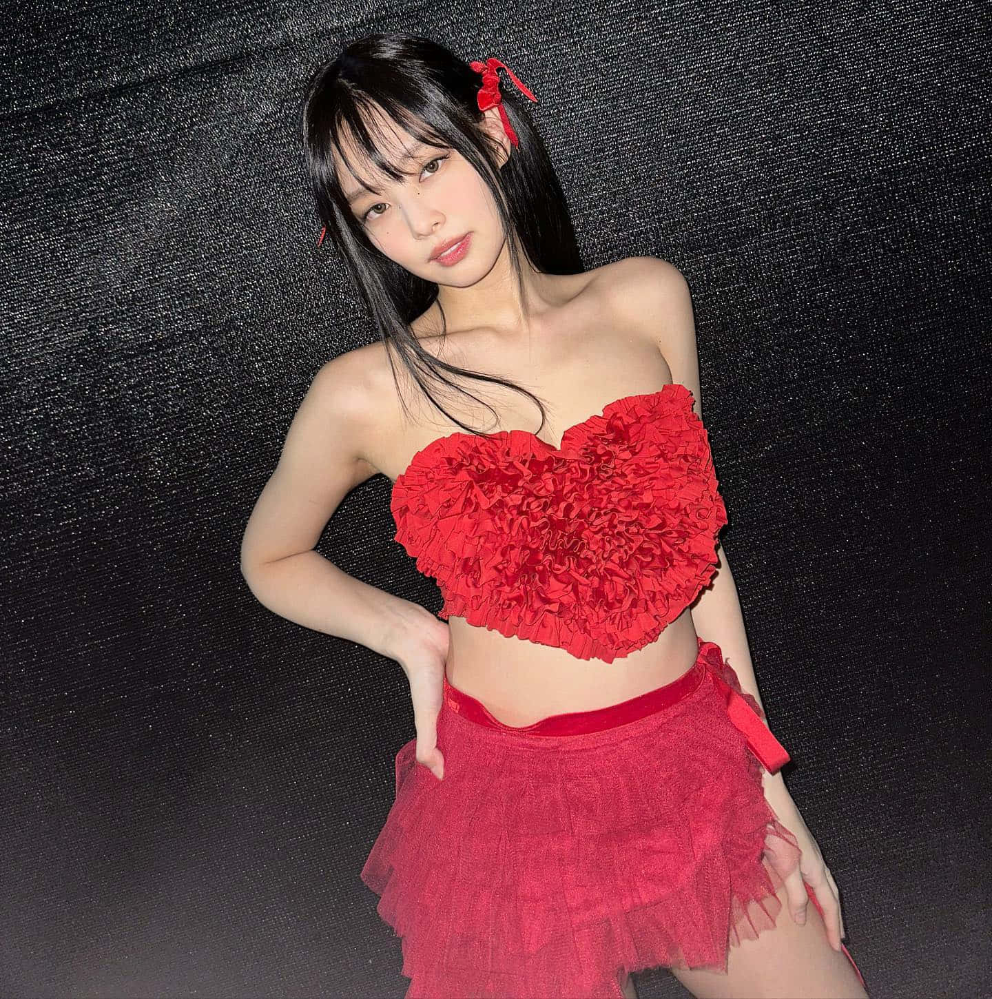 Jennie Kim 穿紅心禮服性感照 壁紙 — 一位年輕女性穿著鮮紅色心形上衣和層疊裙，在深色紋理背景前自信地擺姿勢。