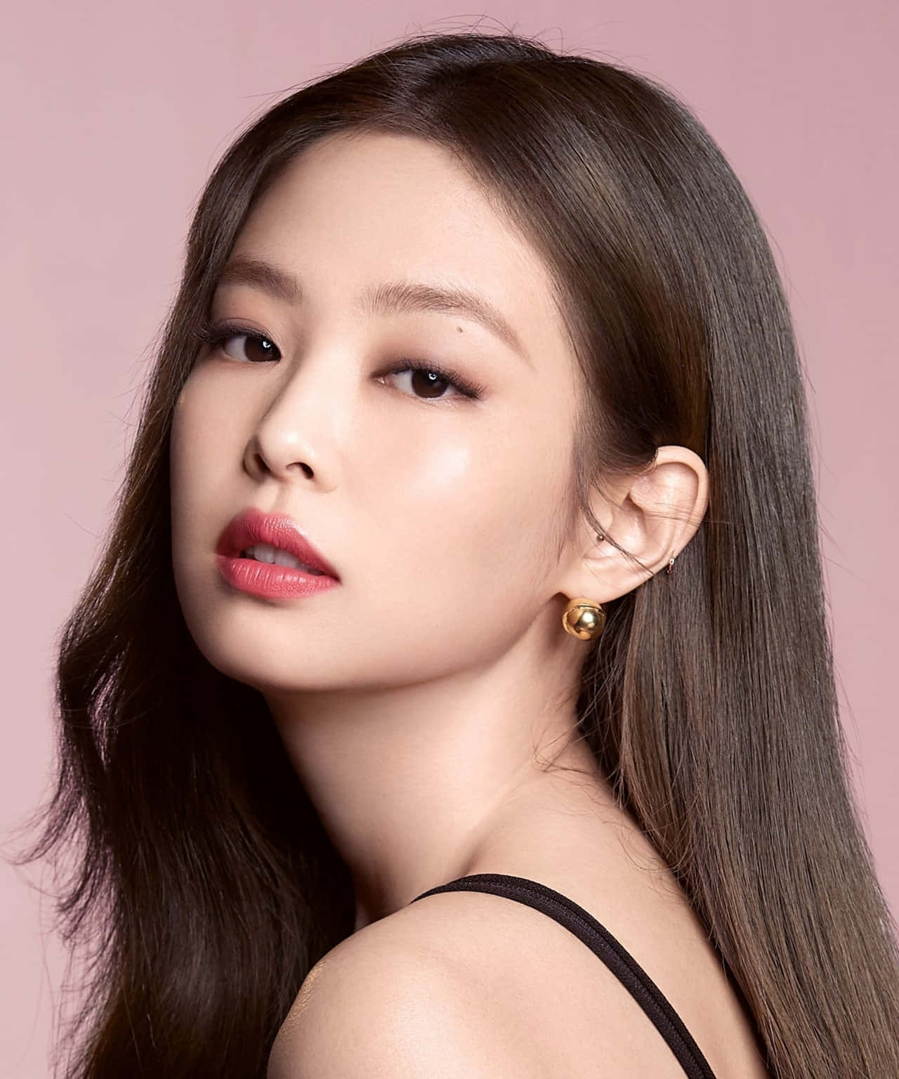 Jennie Kim 粉色背景肖像照 壁紙 — 一位擁有深色長髮和紅唇的女性，在柔和的粉紅色工作室背景下溫柔地凝視。