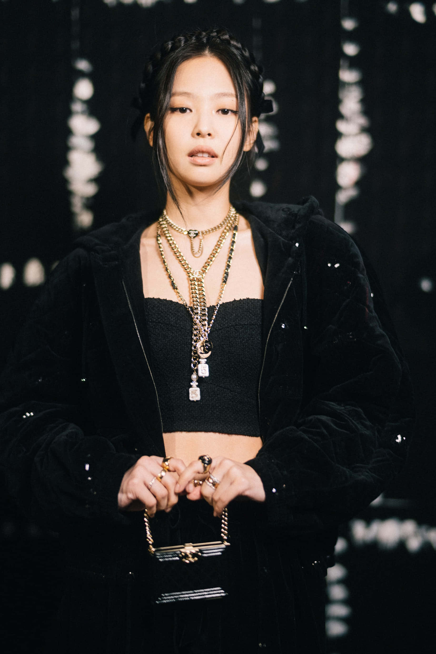 Jennie Kim 黑色美學造型照 壁紙 — 一位年輕女性身穿黑色天鵝絨服飾，搭配多層金色首飾，在帶有白色潑濺的深色抽象背景前擺姿勢。