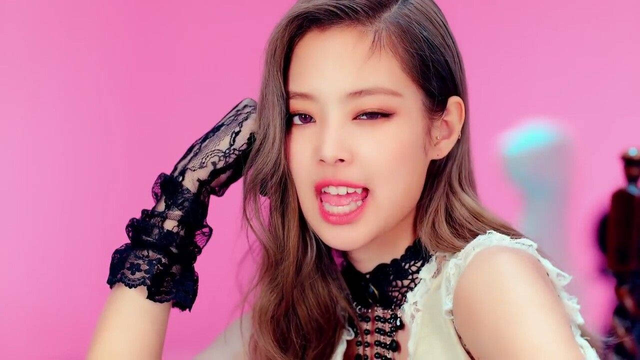 JENNIE《Savage》音樂錄影帶 壁紙 — 一位長棕髮的年輕女性，在充滿活力的粉紅色背景前，戴著黑色蕾絲手套，穿著白色上衣。