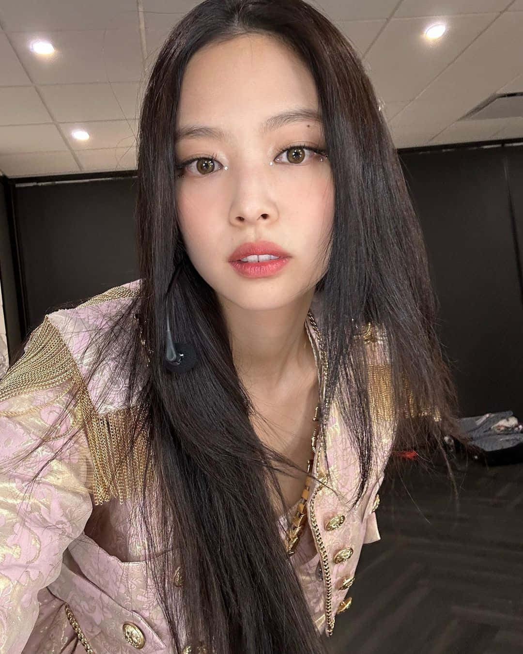 Jennie 自拍美照 壁紙 — 一位長黑髮女性在室內穿著粉紅和金色裝飾外套的 close-up 自拍。