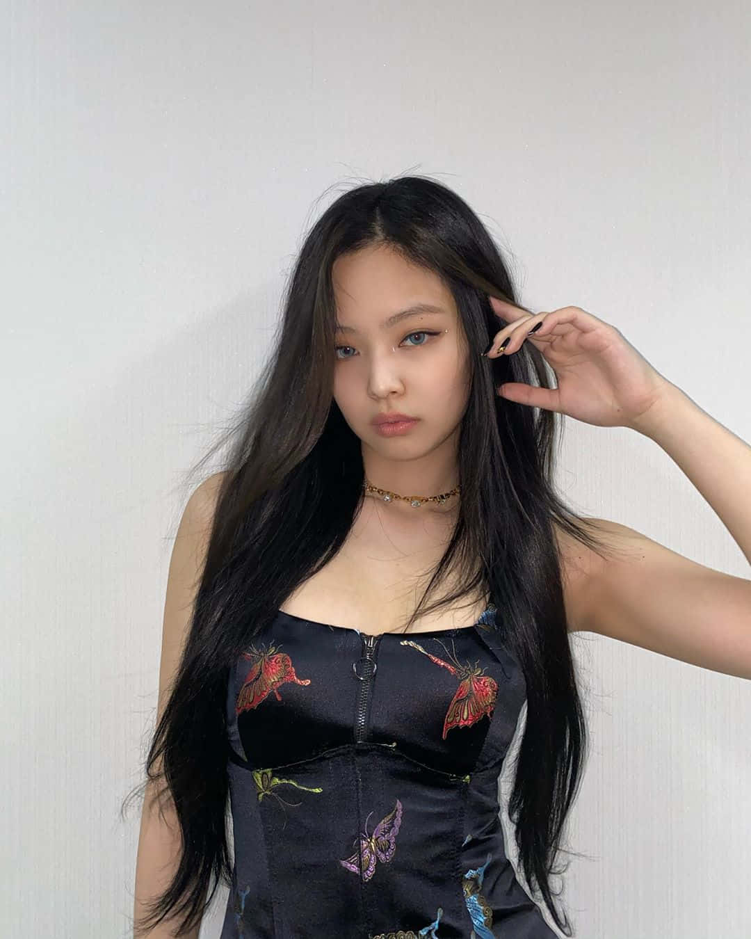 Jennie 長髮美照 壁紙 — 一位長黑髮的年輕女性穿著黑色蝴蝶圖案上衣，背景是純白牆壁。
