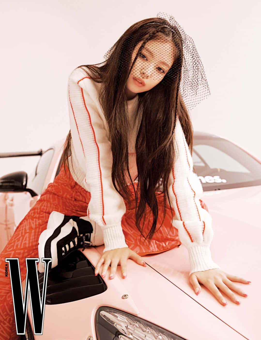 Jennie為W雜誌拍攝的橘白時尚照 壁紙 — 一位長黑髮、戴黑色面紗的女性在攝影棚內俯身於一輛粉紅色跑車上。