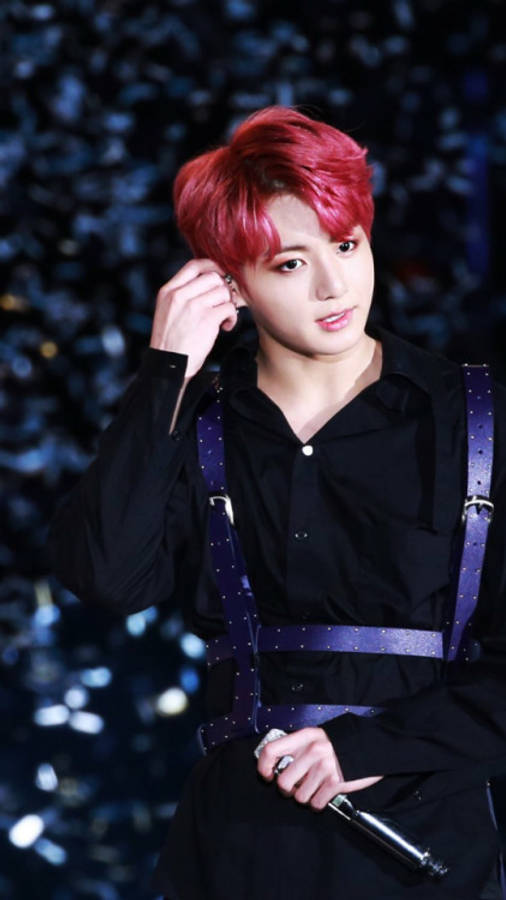 Jeon Jungkook 紅髮造型 壁紙 — 一位擁有鮮豔紅髮和黑色服裝的表演者，在閃爍的藍色背景下手持麥克風。