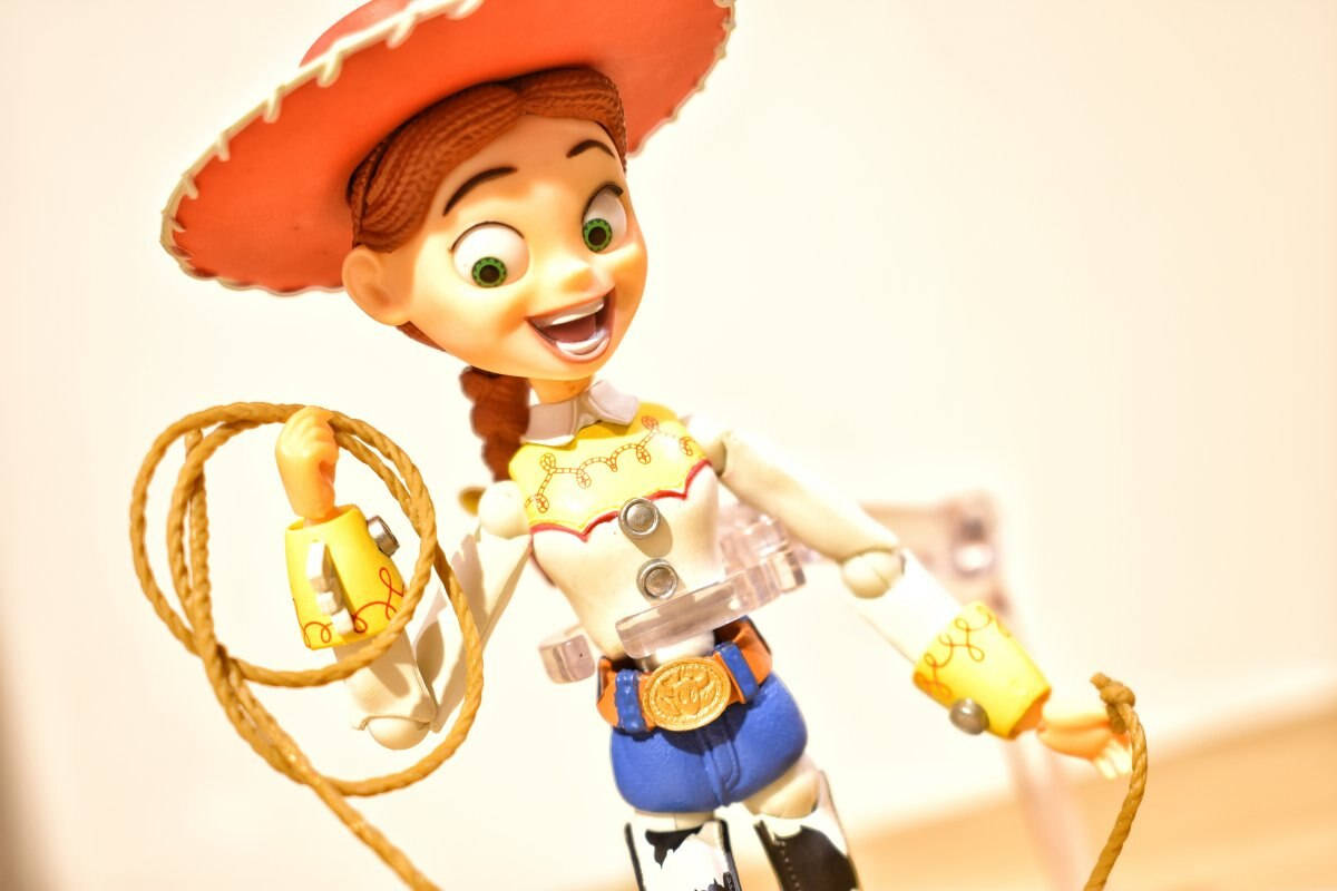 Jessie Toy Story 行動人偶 壁紙 — 一個來自《反斗奇兵》的開心 Jessie 公仔，手持套索，在柔和模糊的背景前燦爛地微笑。