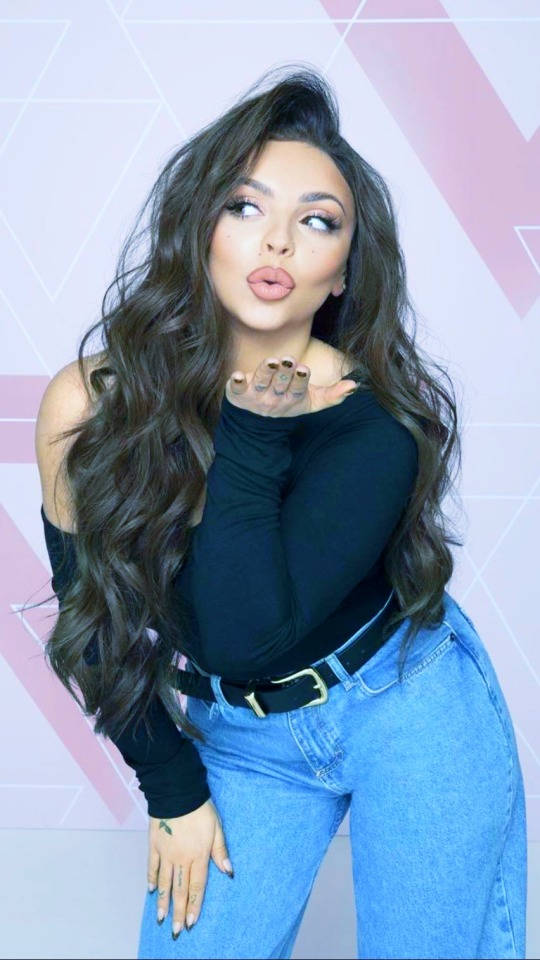 Jesy Nelson 美學風格照 壁紙 — 一位長捲髮的女性向粉紅色幾何圖案牆壁送飛吻。