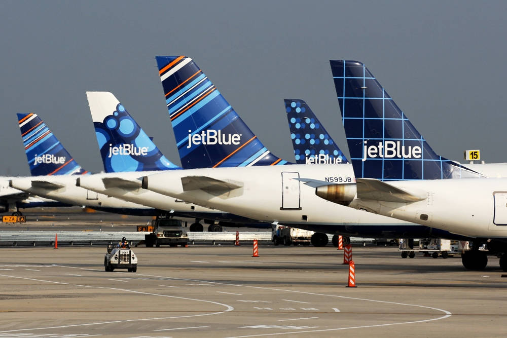 JetBlue航空公司的機翼尾翼印花圖案 壁紙 — 一排捷藍航空飛機停泊在機場閘口，色彩繽紛的機尾朝前，天空多雲。