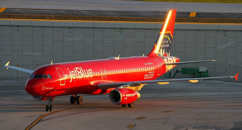JetBlue航空紅色飛機 壁紙 — 一架鮮紅色的JetBlue空中巴士A320在黃金時段於機場停機坪滑行，溫暖的陽光突顯其拋光的機身。