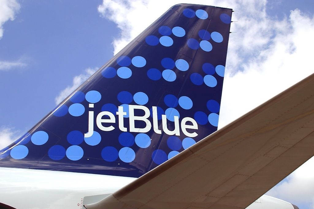 JetBlue 飛機尾翼特寫，帶有藍色波點，背景是藍天和白雲。