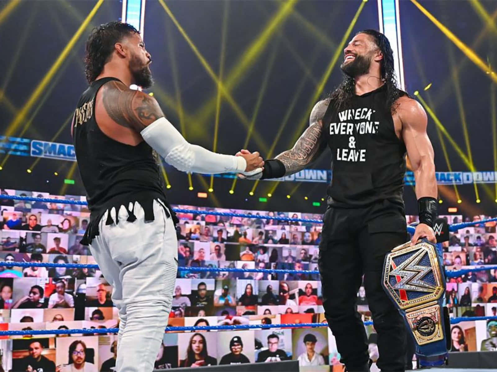 Jey Uso 與 Roman Reigns 握手 壁紙 — 兩位WWE摔角手在擂台上握手，其中一人手持冠軍腰帶，虛擬粉絲從他們身後的屏幕觀看。