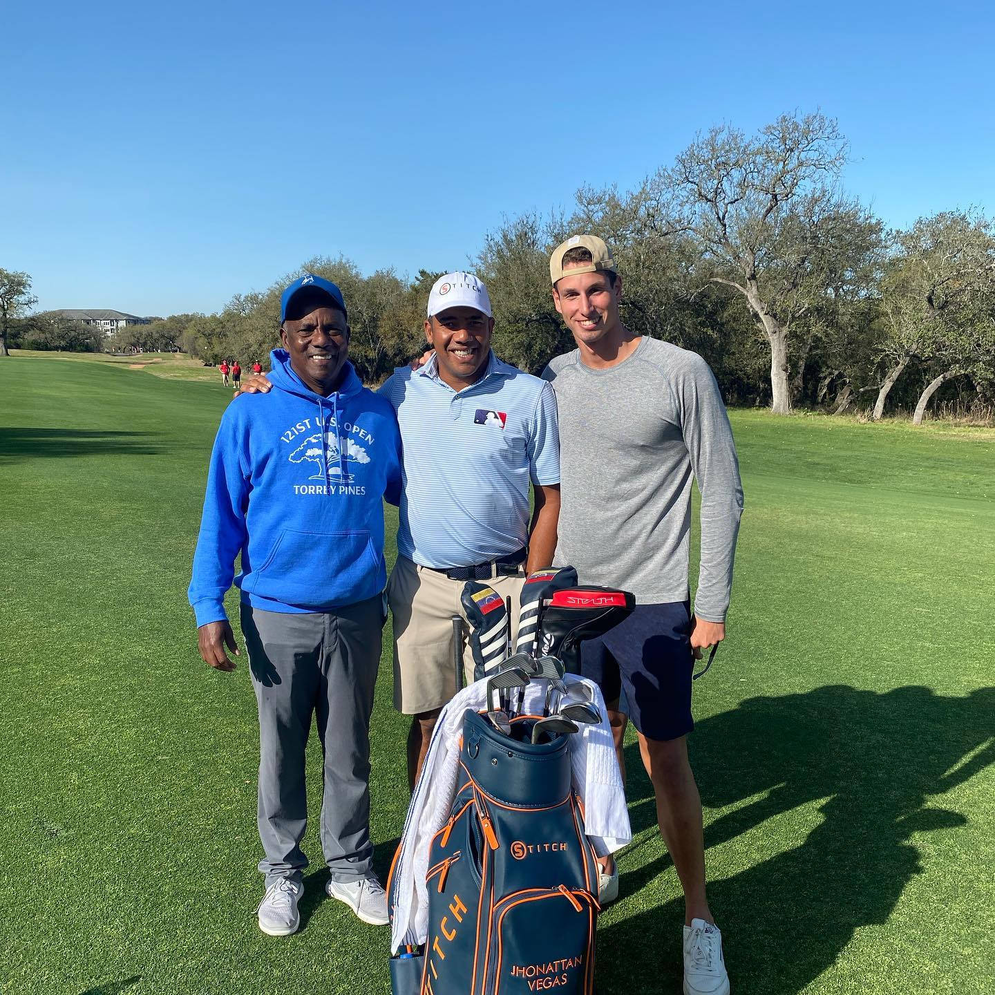 Jhonattan Vegas 與兩位高爾夫球手 壁紙 — 三位微笑嘅男士喺陽光普照嘅高爾夫球場上，中間放住一個高爾夫球袋一齊擺甫士。
