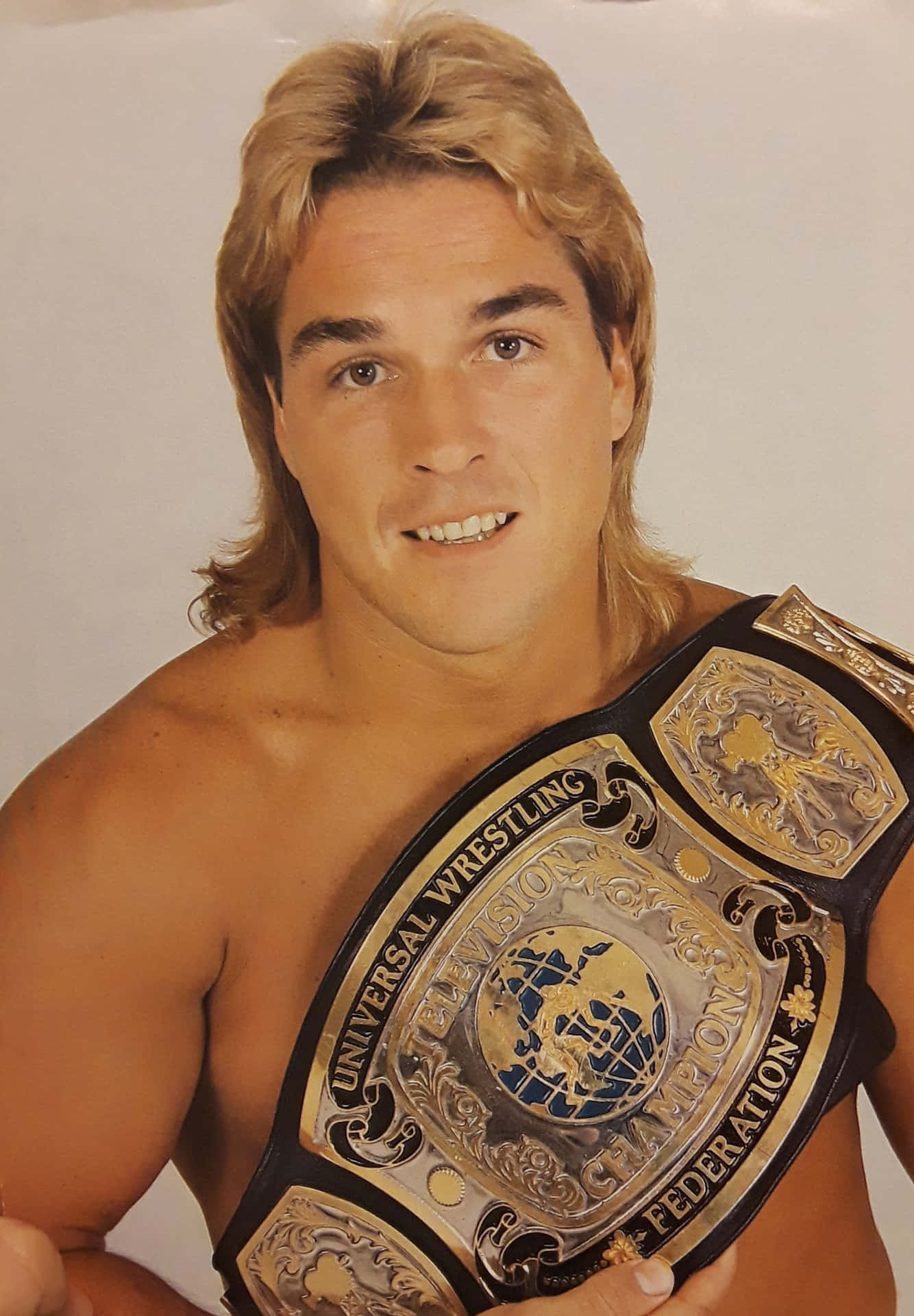  壁紙 — 一位肌肉發達的金髮男子，在純色背景前自豪地舉起閃亮的Universal Wrestling Federation冠軍腰帶。