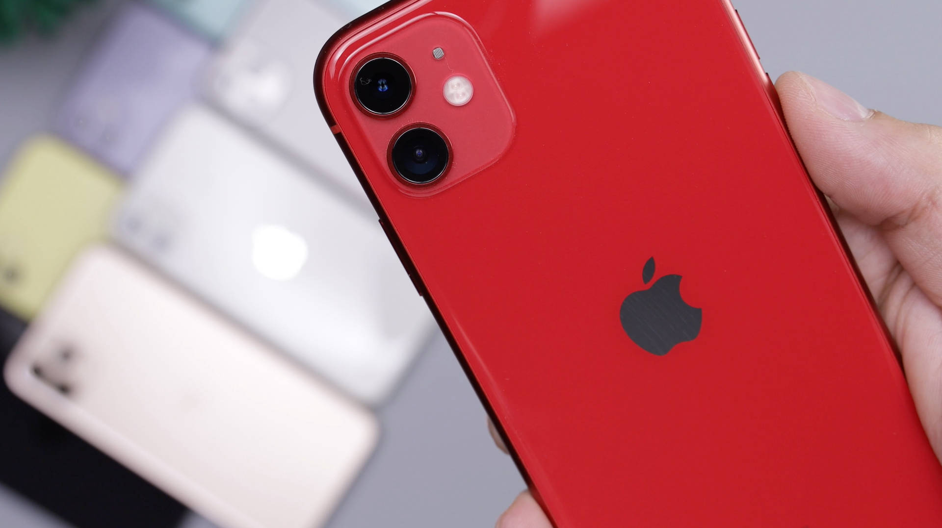 手拿著紅色iPhone 11，其他電話在背景模糊。