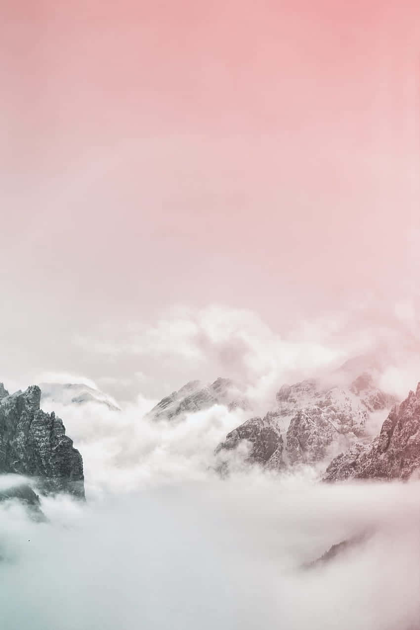  壁紙 — 積雪的山峰在夢幻般的粉紅色天空下穿過柔軟的雲層。