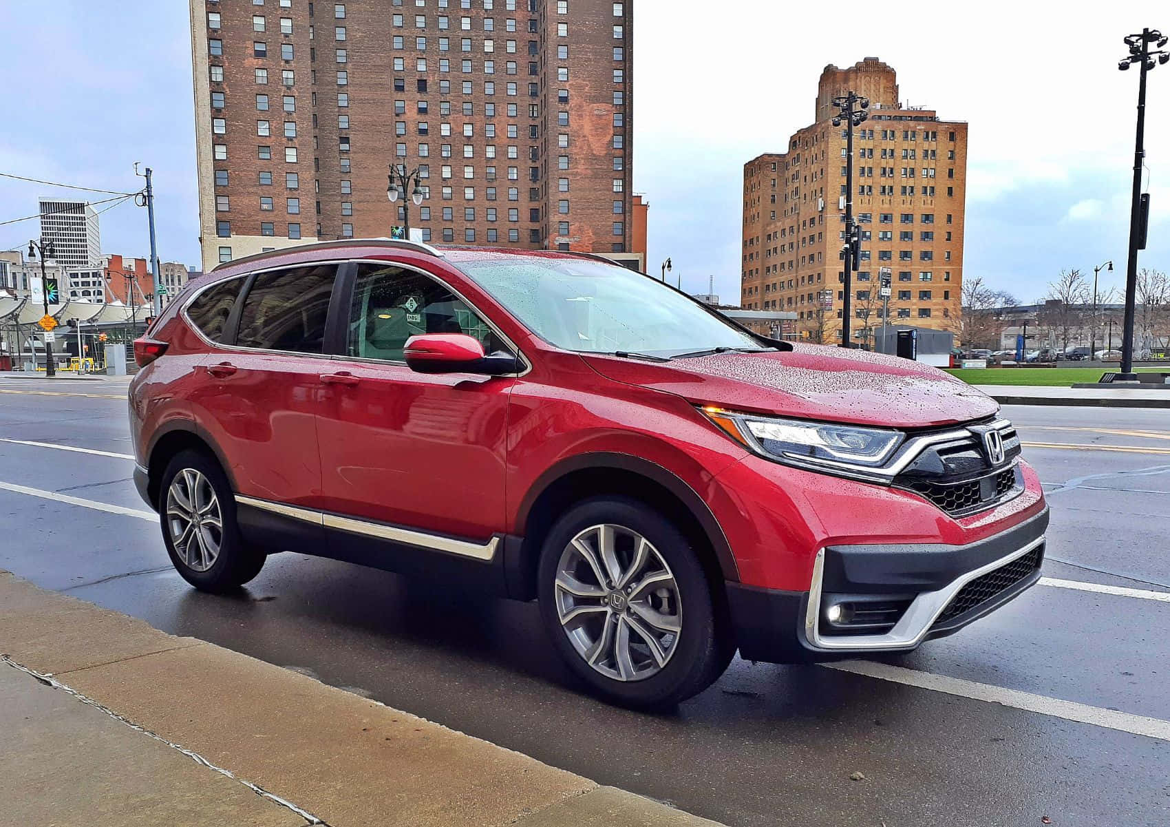 Honda Cr-v 桌布 壁紙 — 一架亮紅色本田CRV SUV停泊在潮濕的城市街道上，背景是磚砌建築，天空多雲。