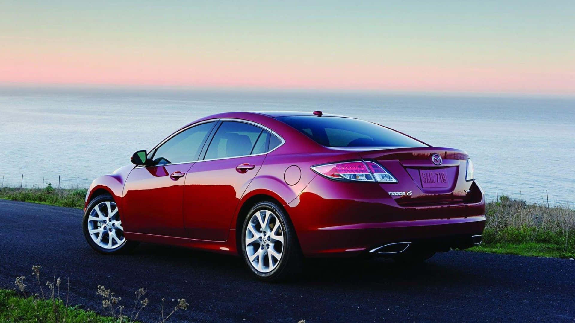 Mazda 6 桌布 壁紙 — 一架亮紅色Mazda 6房車停泊在日落時分的海岸公路上，背後是海洋地平線。