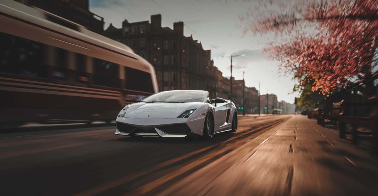 Lamborghini Gallardo 桌布 壁紙 — 一架流線型白色林寶堅尼Gallardo Spyder在日落時分，伴隨著櫻花和移動中模糊的電車，在城市的街道上飛馳。