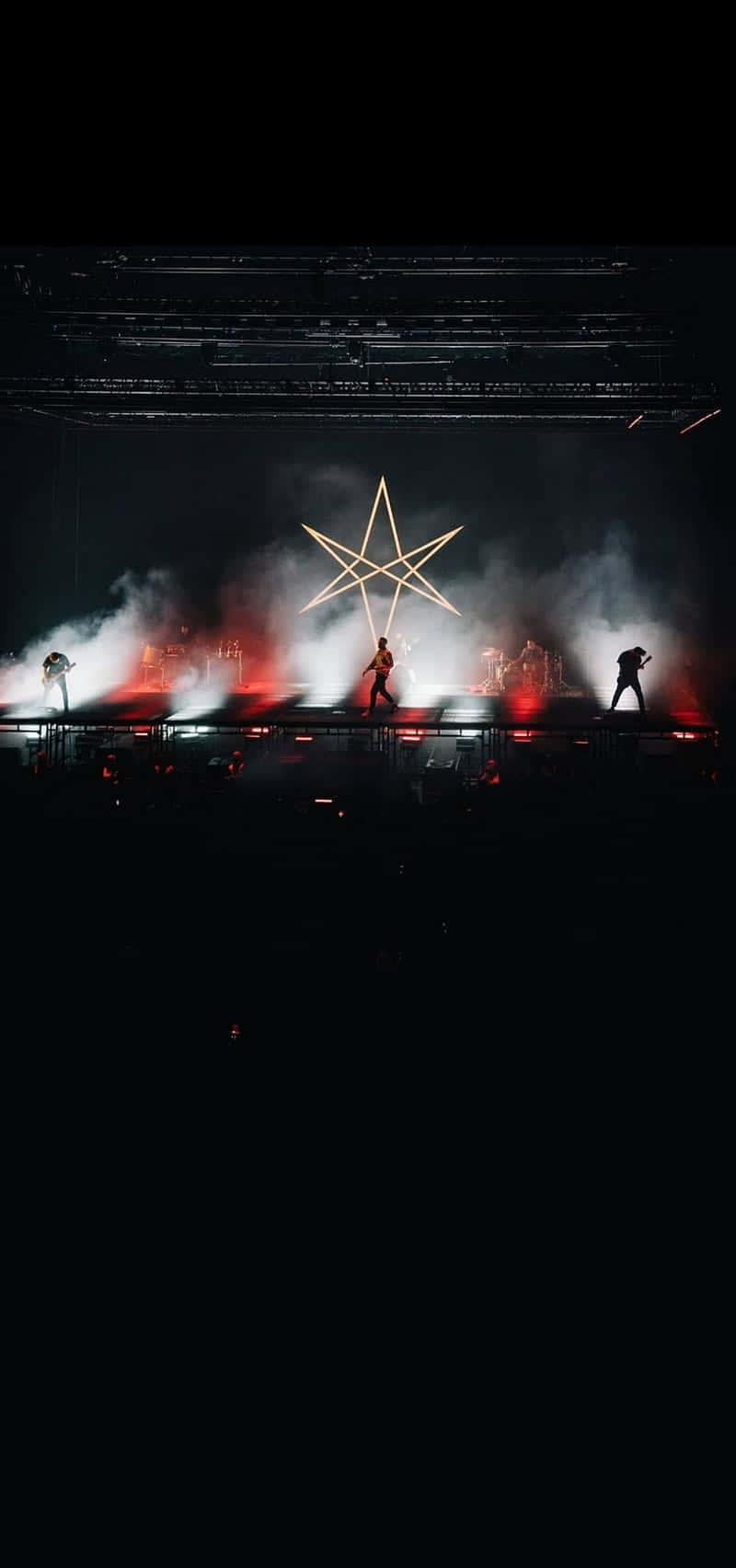  壁紙 — 剪影音樂家在黑暗舞台上表演，舞台由紅燈和發光的星形結構照亮。