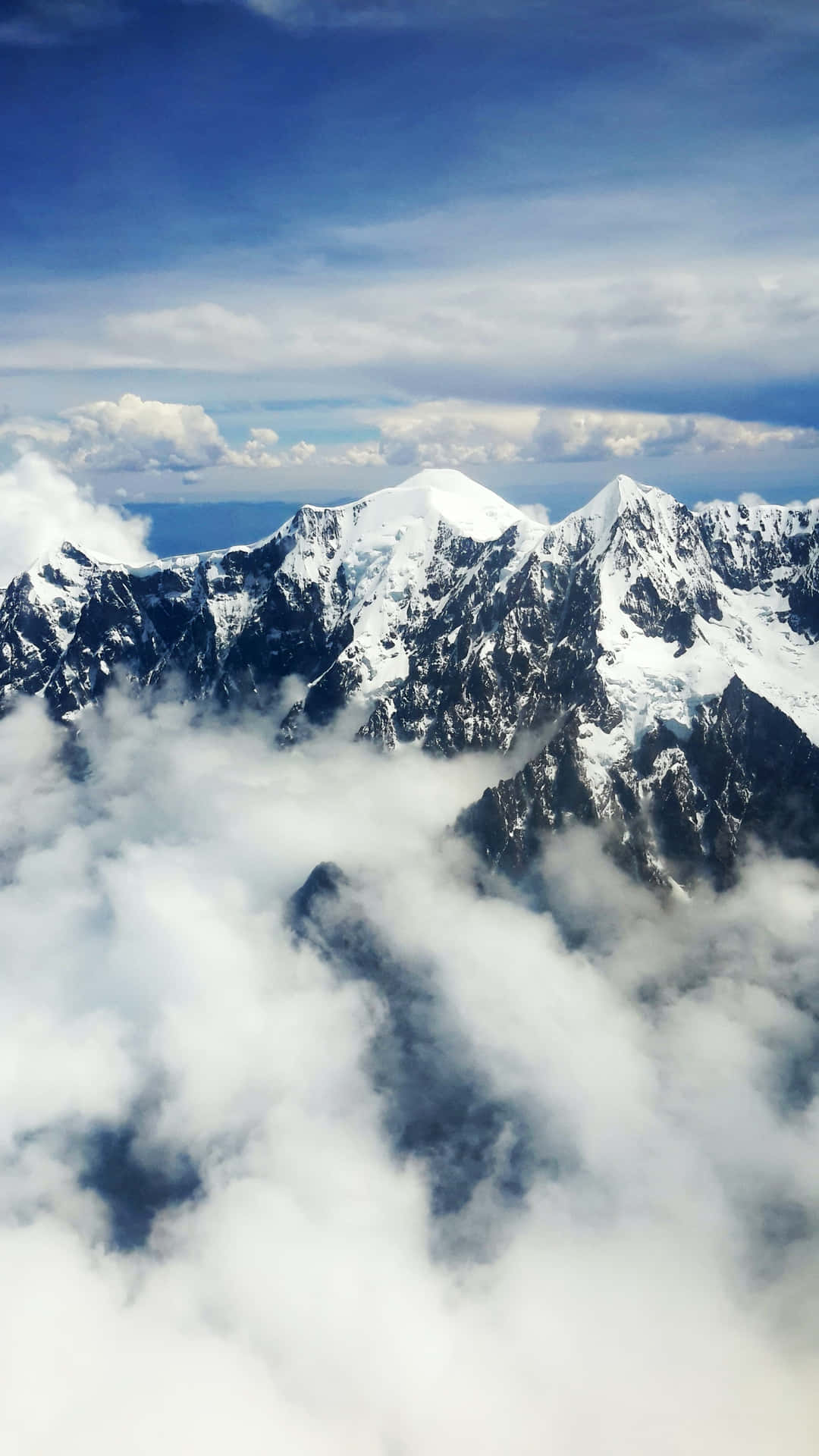積雪的山峰在藍天下聳立於雲層之上。