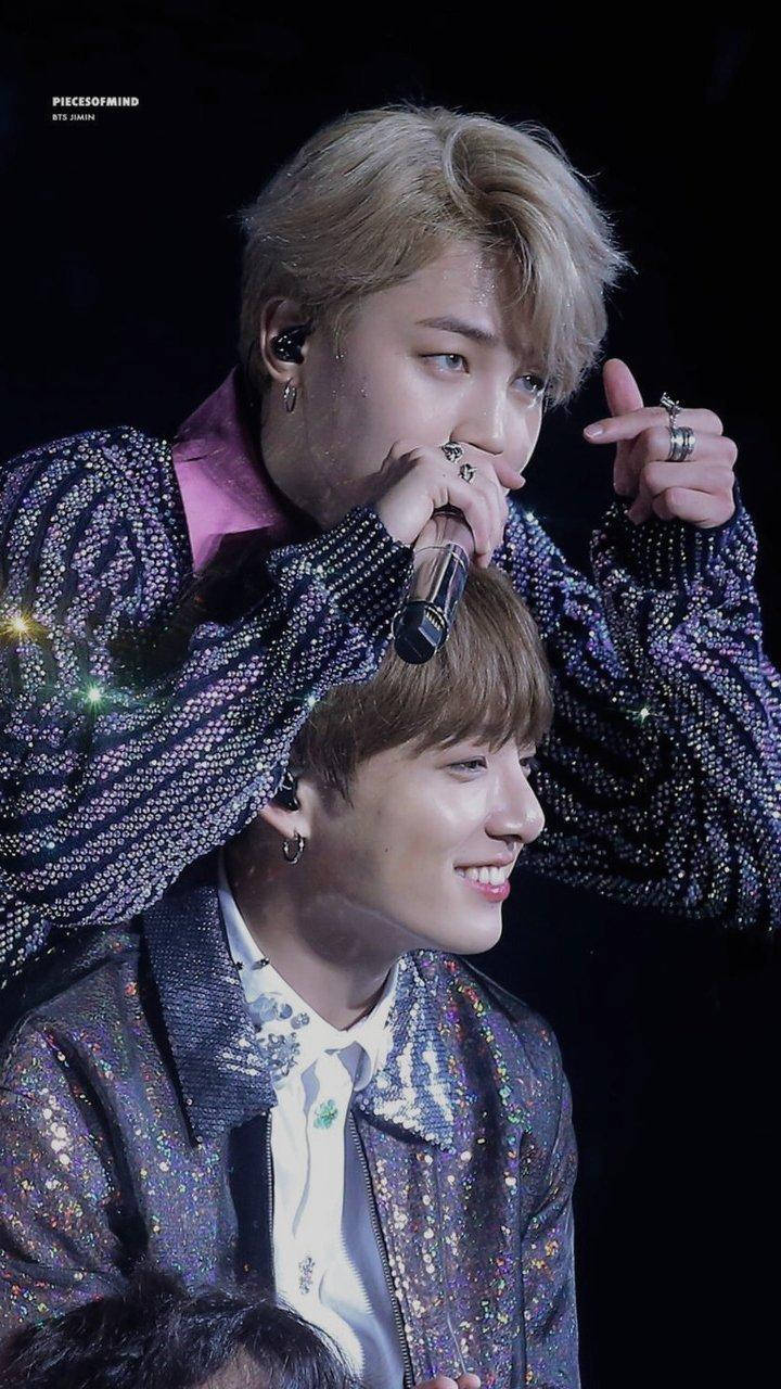 Jikook 笑著指著 壁紙 — 兩位身穿閃亮外套的男性表演者在舞台燈光下，帶著強烈的表情對著麥克風唱歌。