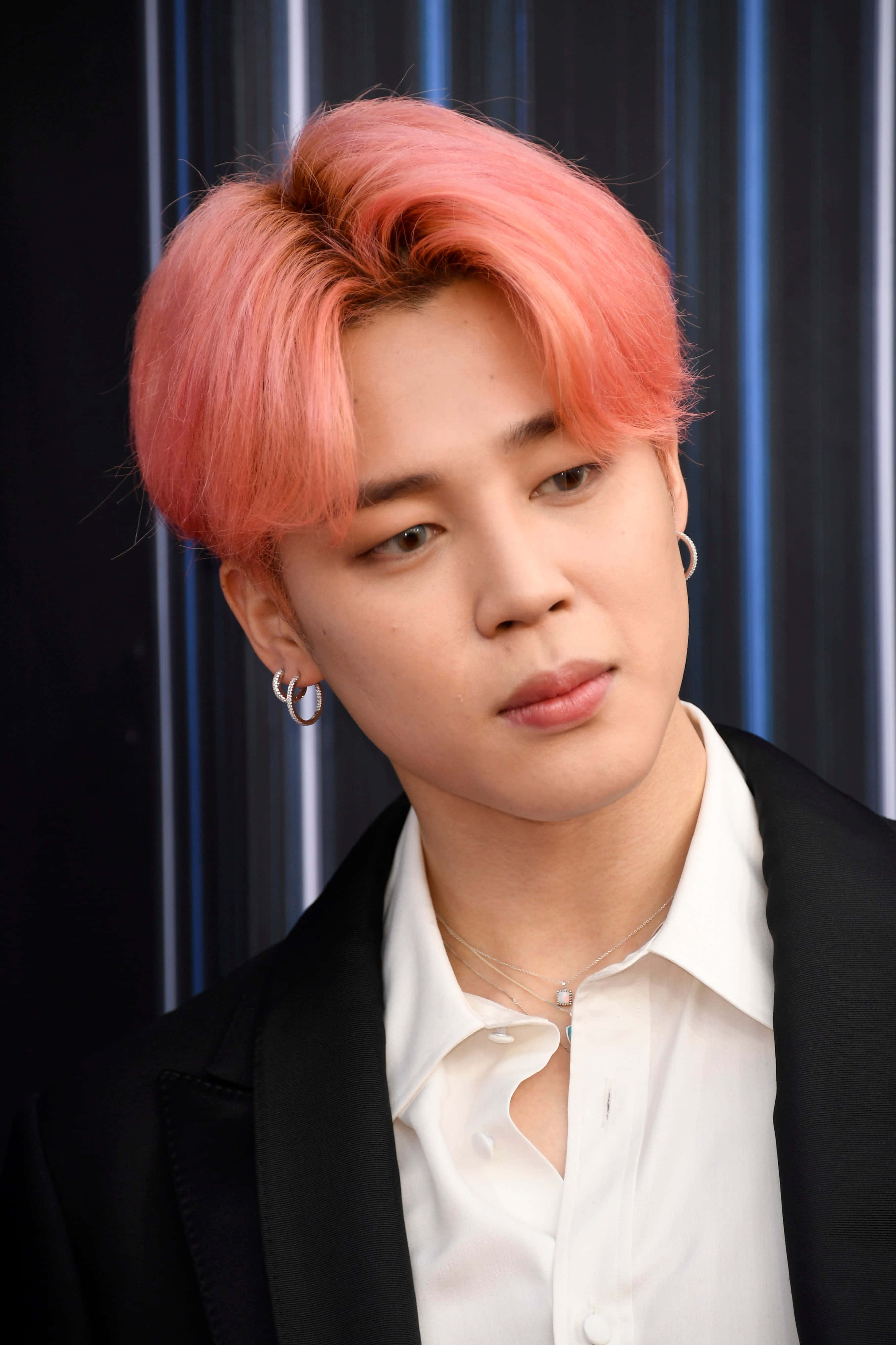 Jimin 穿紅色西裝風采翩翩 壁紙 — 一位年輕男子，擁有鮮豔的粉紅色頭髮和銀色耳環，在深藍色條紋背景下若有所思地凝視。