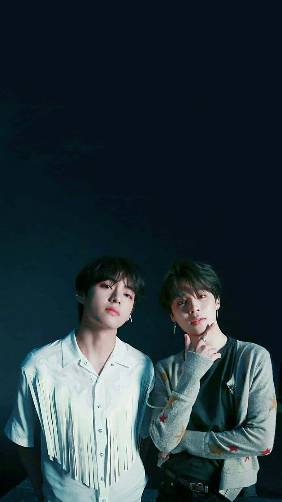 Jimin 與 V BTS 精緻手機壁紙 壁紙 — 兩名年輕男子在冷藍色燈光下，於深色背景前擺姿勢，一人穿著流蘇襯衫，另一人穿著圖案毛衣。