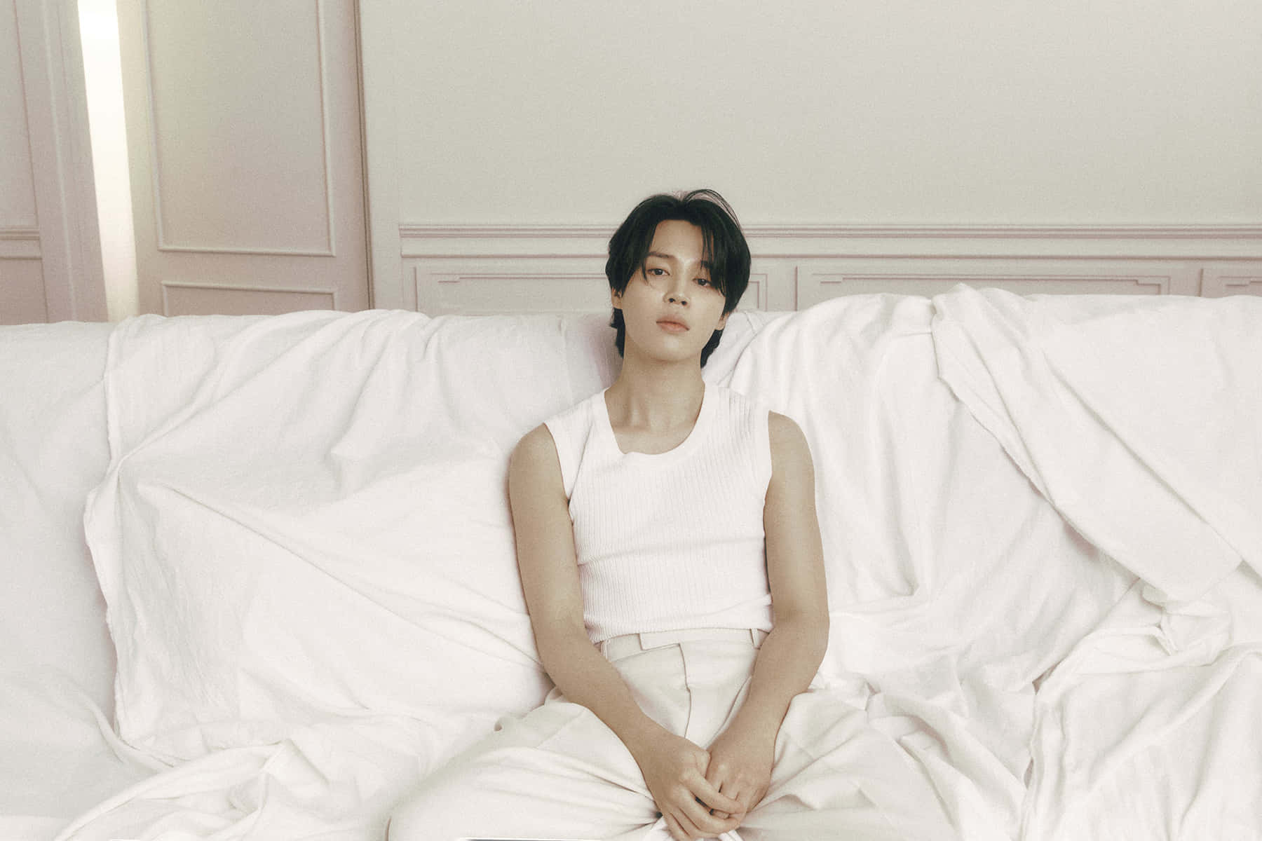 Jimin揮手道別 壁紙 — 一位身穿白衣的年輕男子在光線柔和的房間裡，平靜地躺在鋪著皺褶白床單的床上。