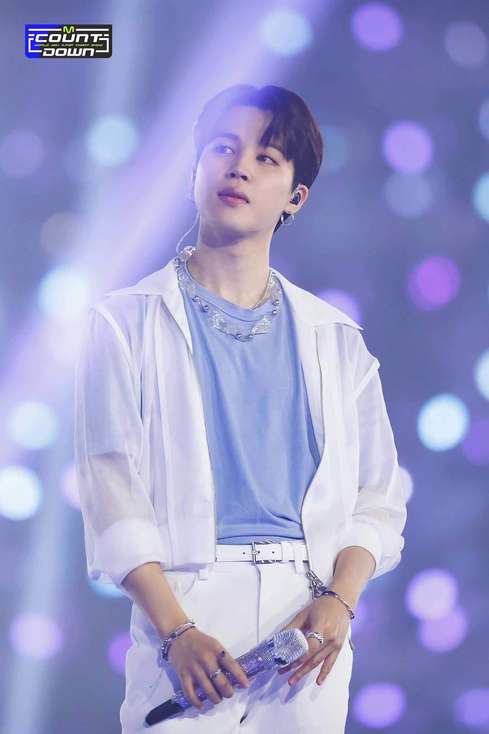 Jimin準備征服音樂產業 壁紙 — 一位身穿白色服裝的年輕男表演者在發光的紫色和藍色舞台燈光下拿著麥克風。