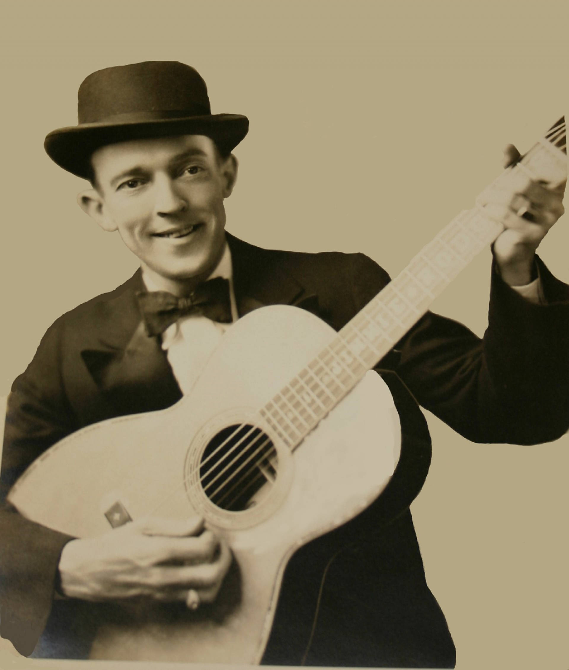 Jimmie Rodgers 古早 Sepia 肖像照 壁紙 — 一位戴著圓頂硬禮帽和領結的微笑男子，在純色懷舊背景前抱著一把原聲結他。