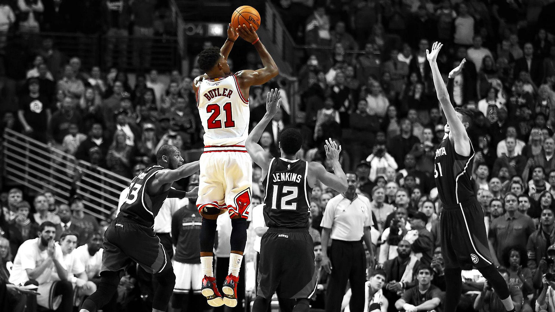 Jimmy Butler 臨門一擊為公牛隊奪勝 壁紙 — 一名身穿白色球衣的籃球運動員跳起投籃，而身穿黑色球衣的防守球員跳起封阻，在高對比度的黑白球場場景中，球和鞋子上有選擇性色彩。