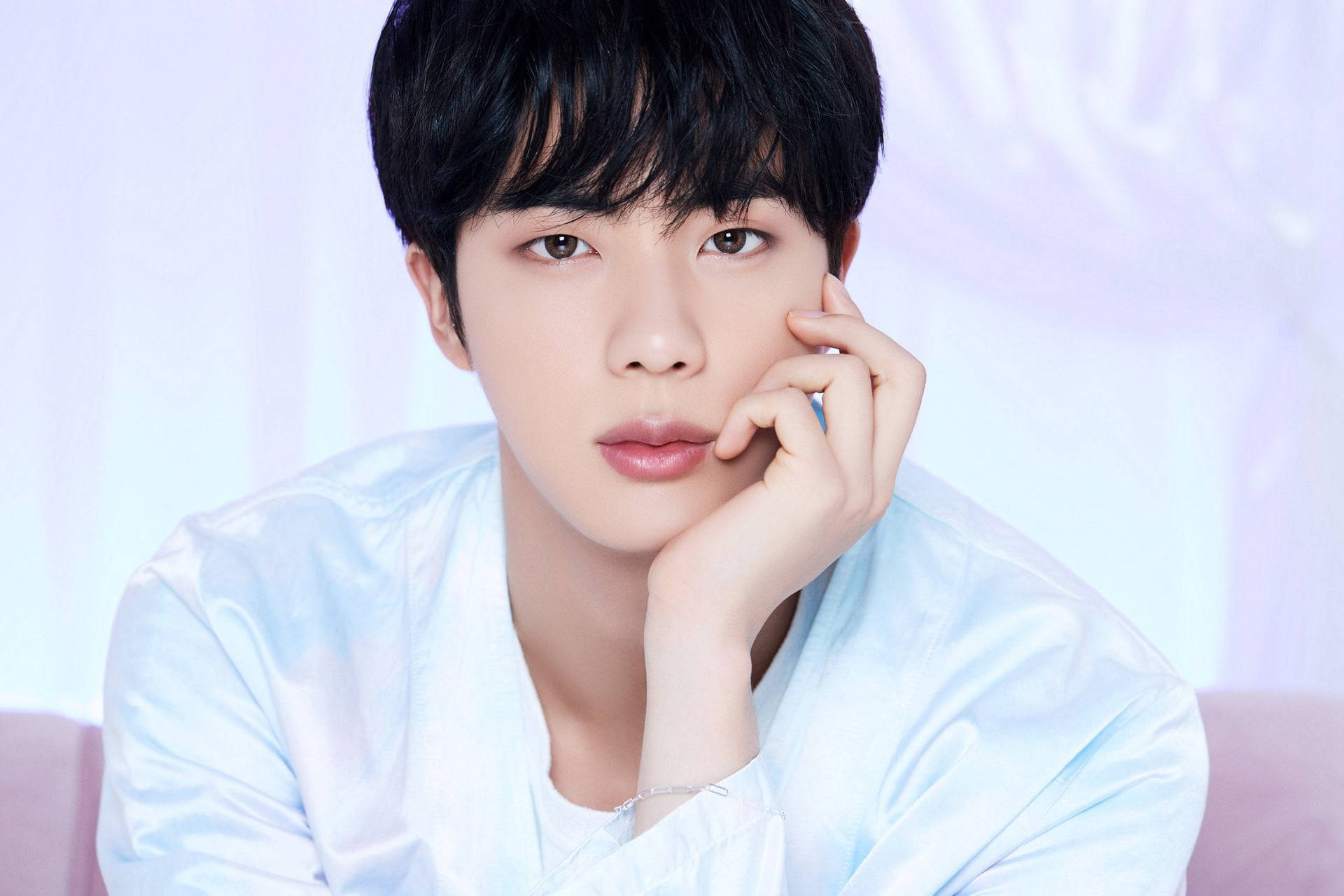 Jin BTS《Life Goes On》概念照 壁紙 — 一位深色頭髮的年輕男子將下巴擱在手上，背景是柔和的粉彩色。