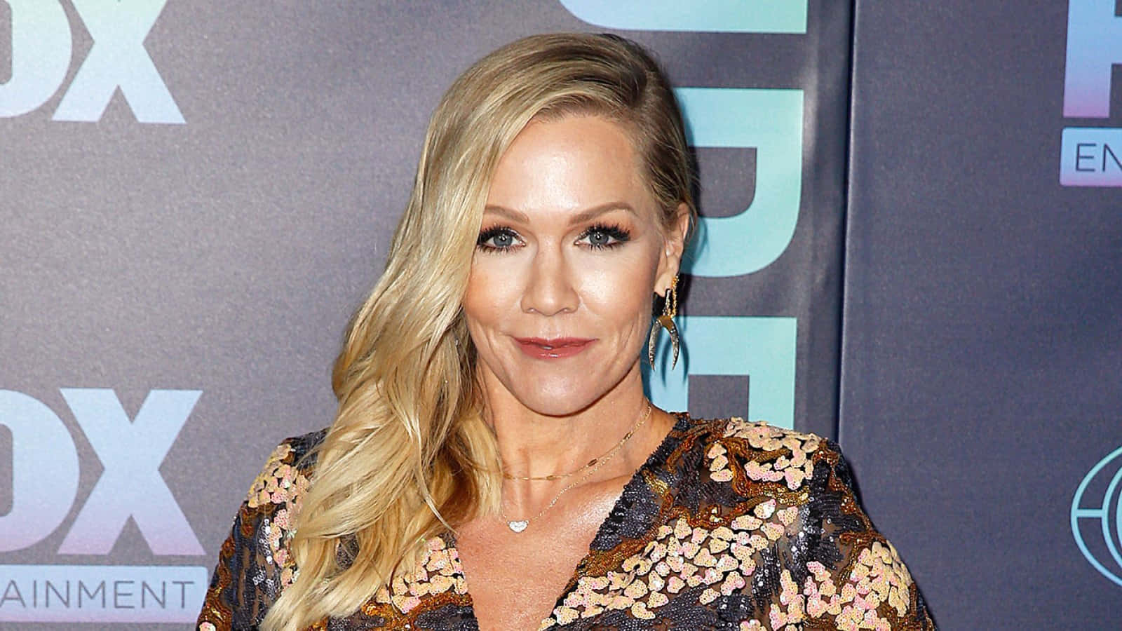 Jennie Garth 桌布 壁紙 — 一位金髮波浪長髮的女性在FOX Entertainment活動中穿著花卉圖案連衣裙對著鏡頭微笑。