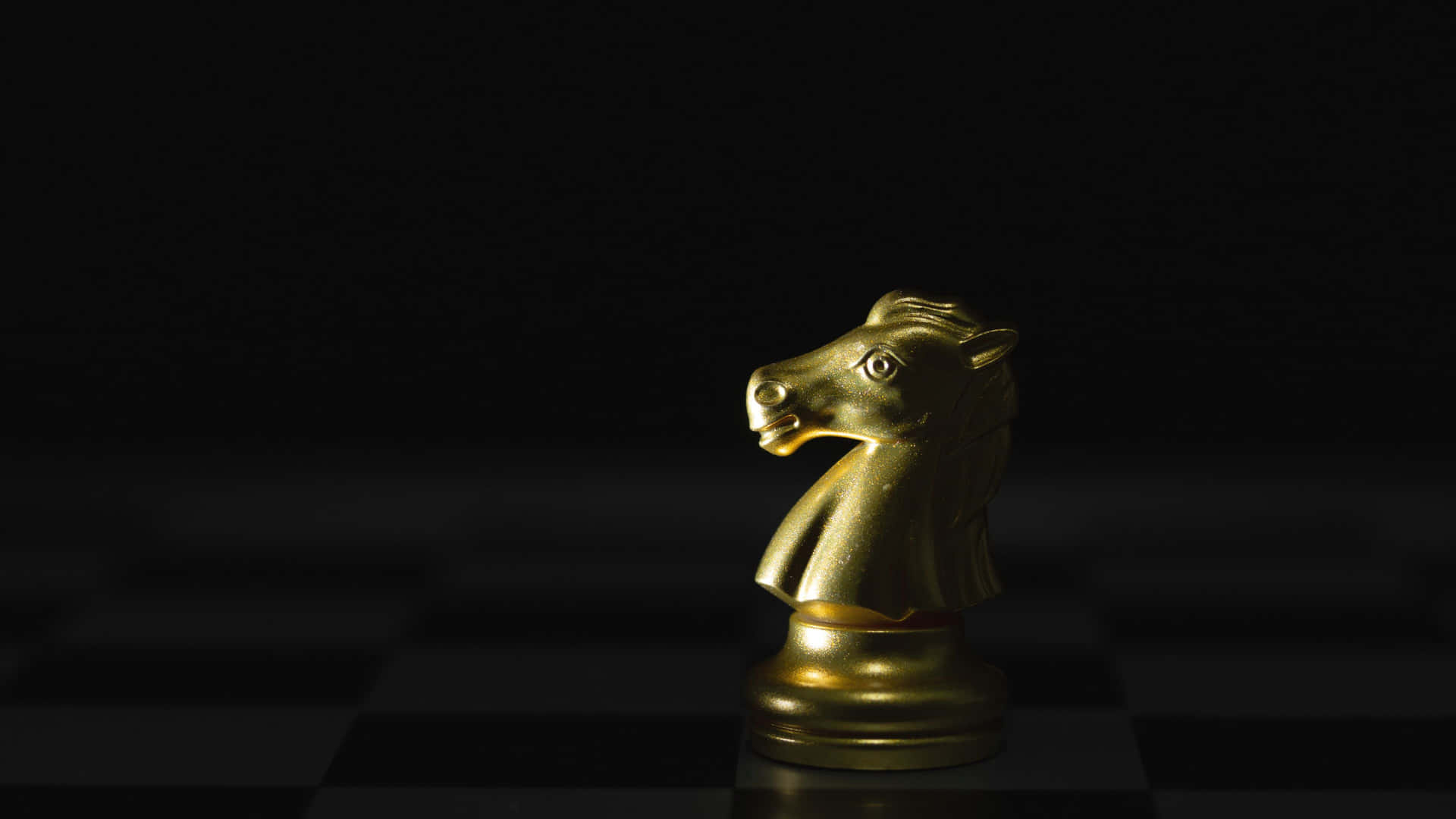  壁紙 — 一個閃閃發光的金色國際象棋騎士獨自站在黑色背景的深色棋盤上。